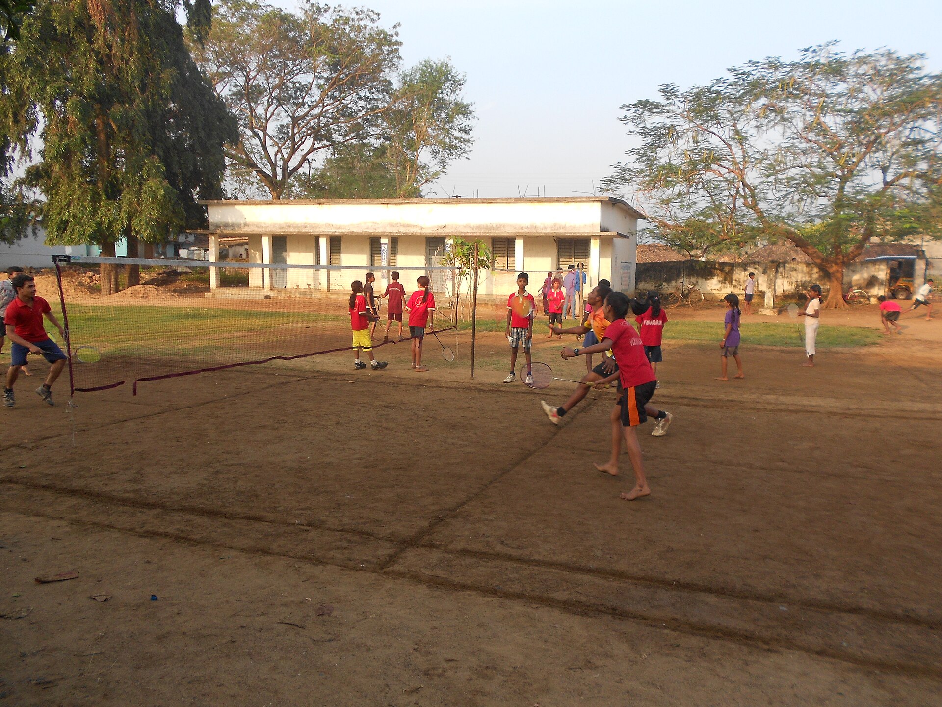 Children practising badminton at an outdoor coaching session on a ground in India