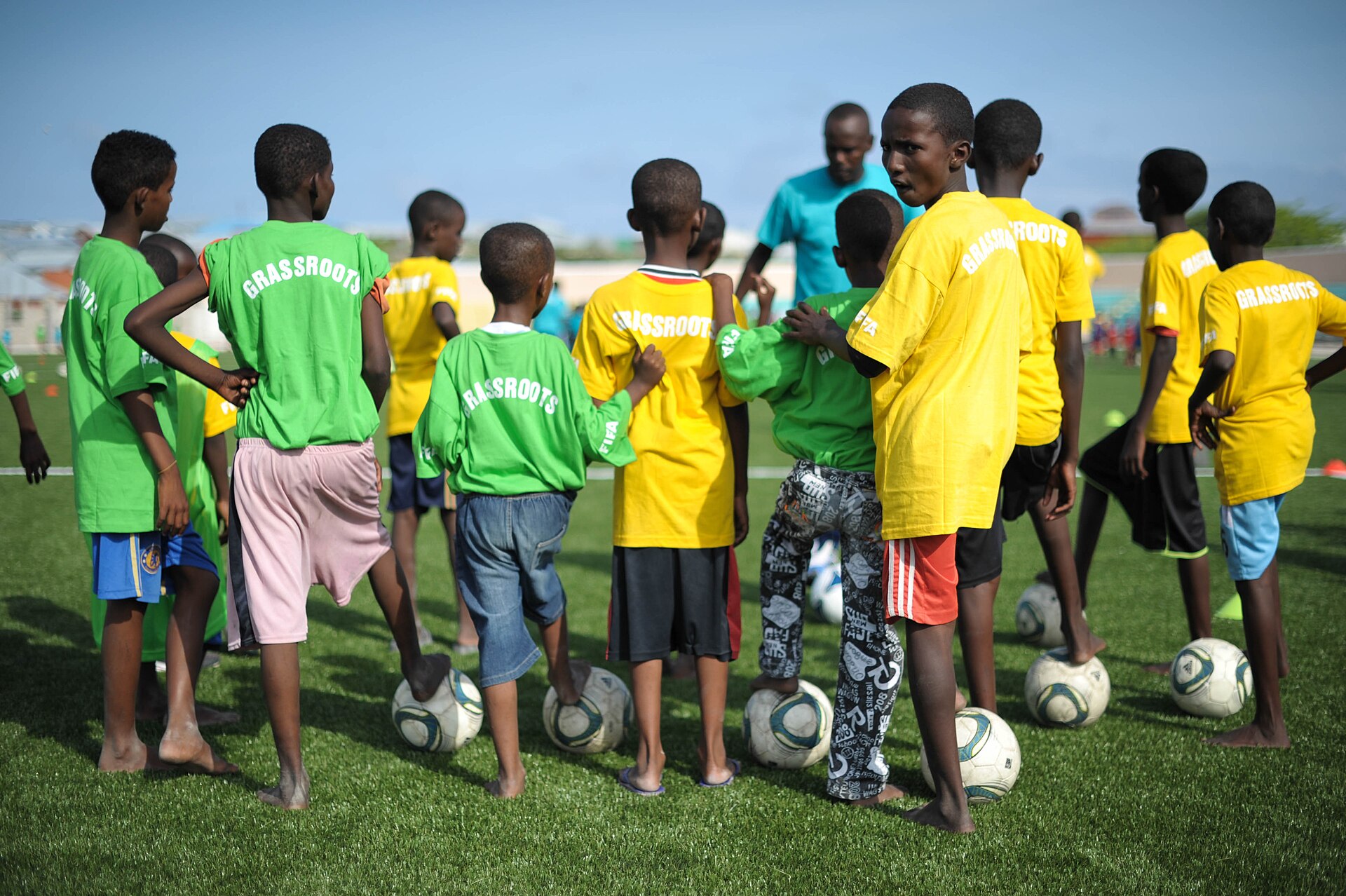 Young football players with balls at their feet listening to a coach during a grassroots training session